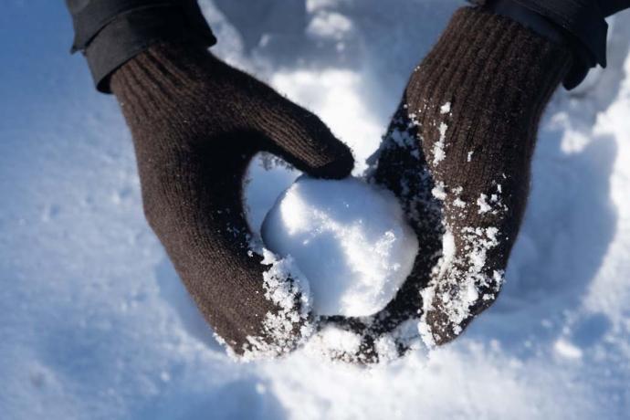 Für jede Schneeballschlacht gewappnet Dunkelbraune Fäustlinge halten Schneeball