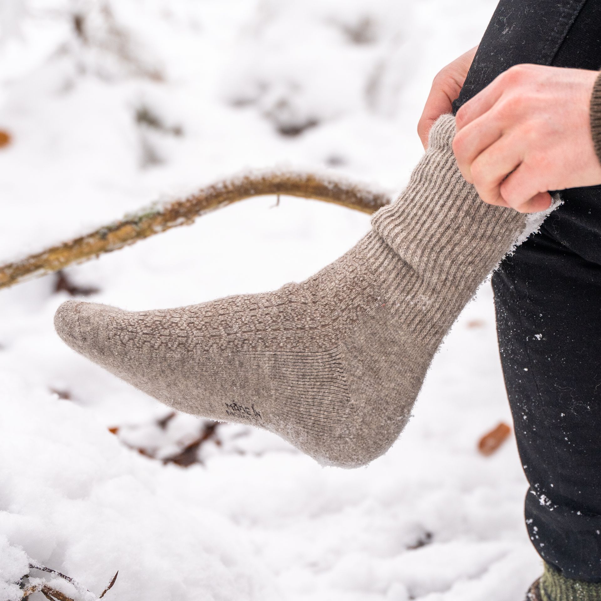 Naturgraue Socken werden in einer schneebedeckten Landschaft angezogen