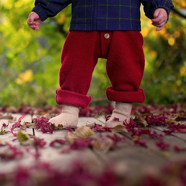 Ein Kleinkind läuft mit Socken über Holzboden voller roter Blätter