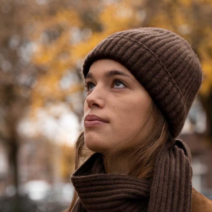 Woman with dark brown scarf and cap looks upwards